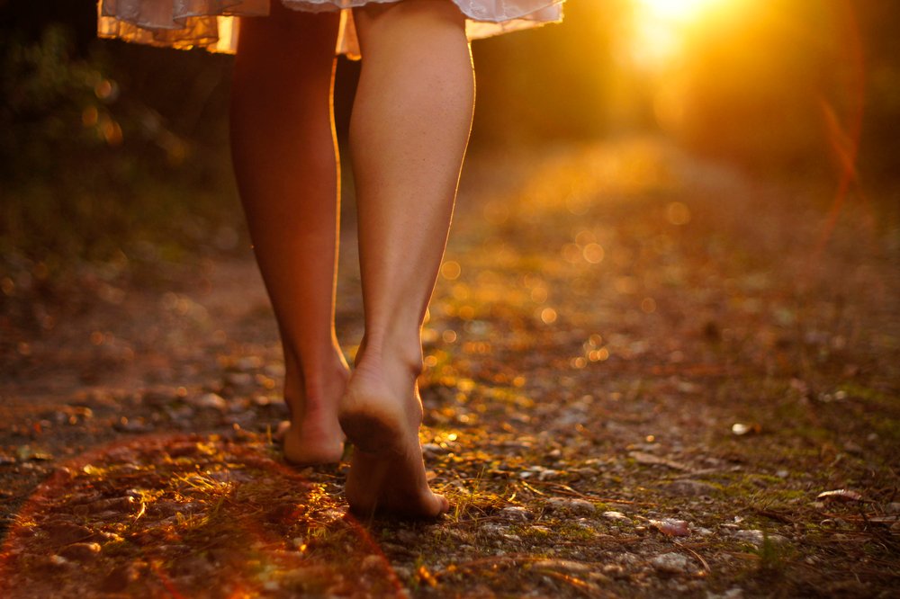 Young female legs walking towards the sunset on a dirt road