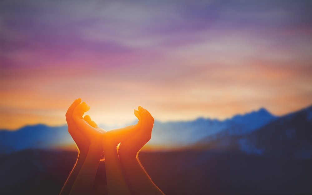 Human hands praying together at dawn time over mountains