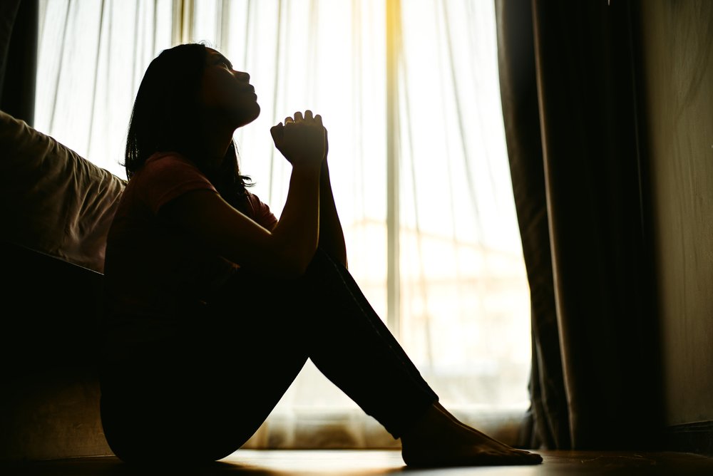 woman sitting near bed looking up praying to god