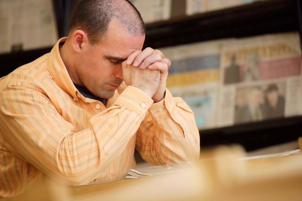 man praying to god with hands joined touching his head