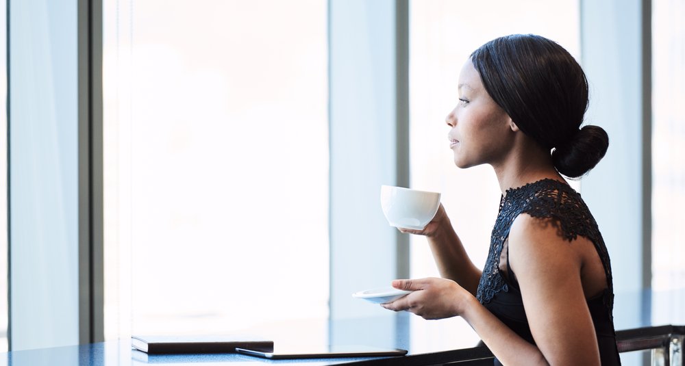 Highly successful young African American woman looking out the window while drinking her morning coffee, while reflecting on her past and thinking about her future.