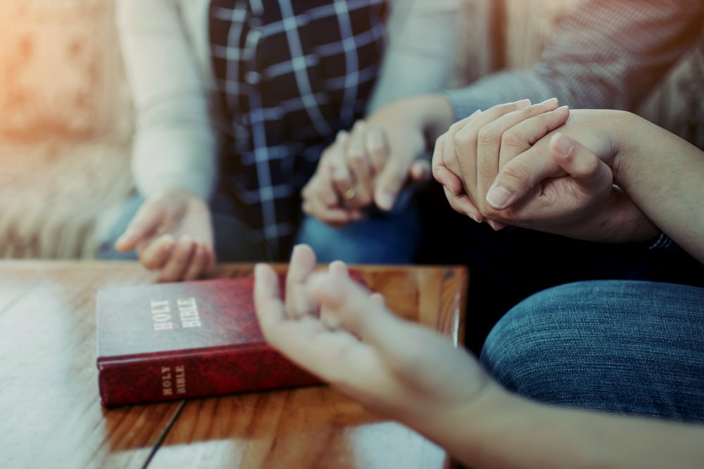 people holding hands with bible on table