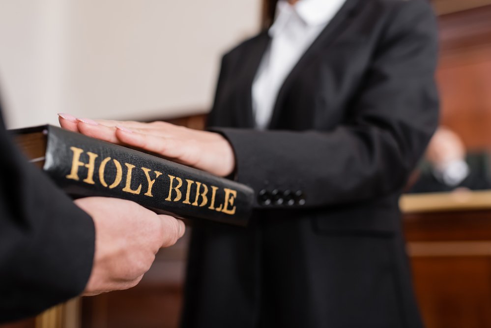 Cropped view of blurred woman giving swear on bible during litigation, witnessing