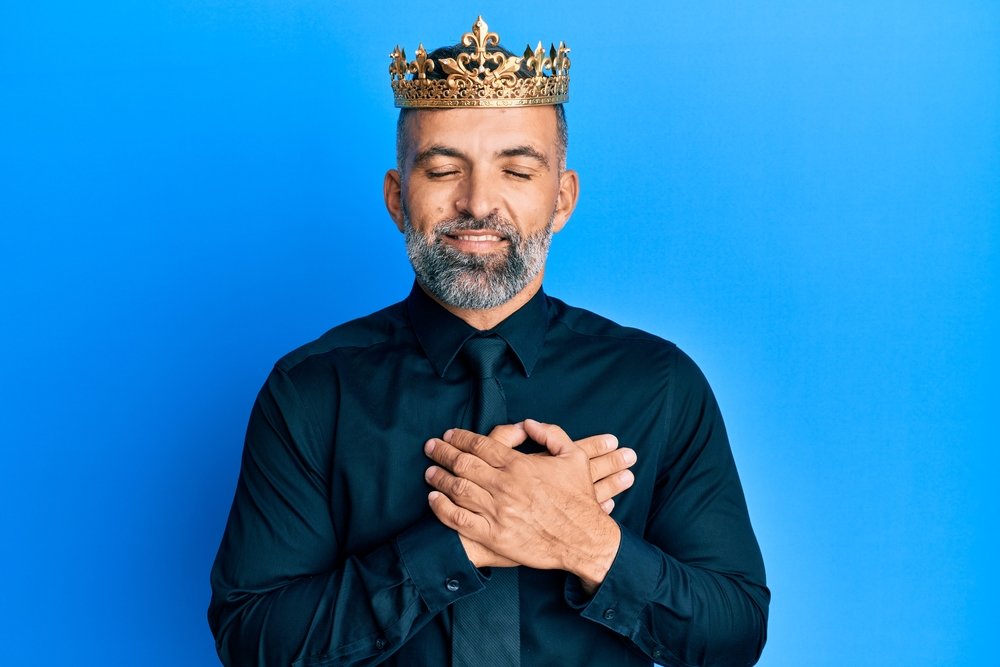 Middle age handsome business man wearing king crown smiling with hands on chest with closed eyes and grateful gesture on face. health concept.