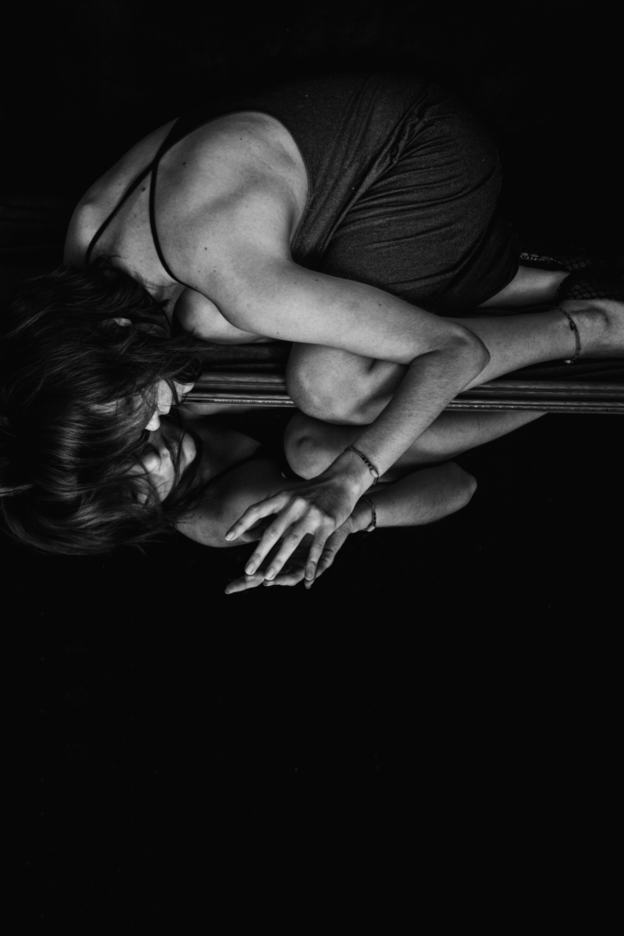 black and white image of woman lying on floor looking at her refection vulnerably