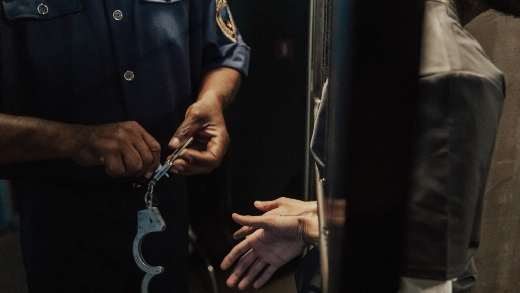 cop with a handcuff in front of a prison cell with a man behind the bars