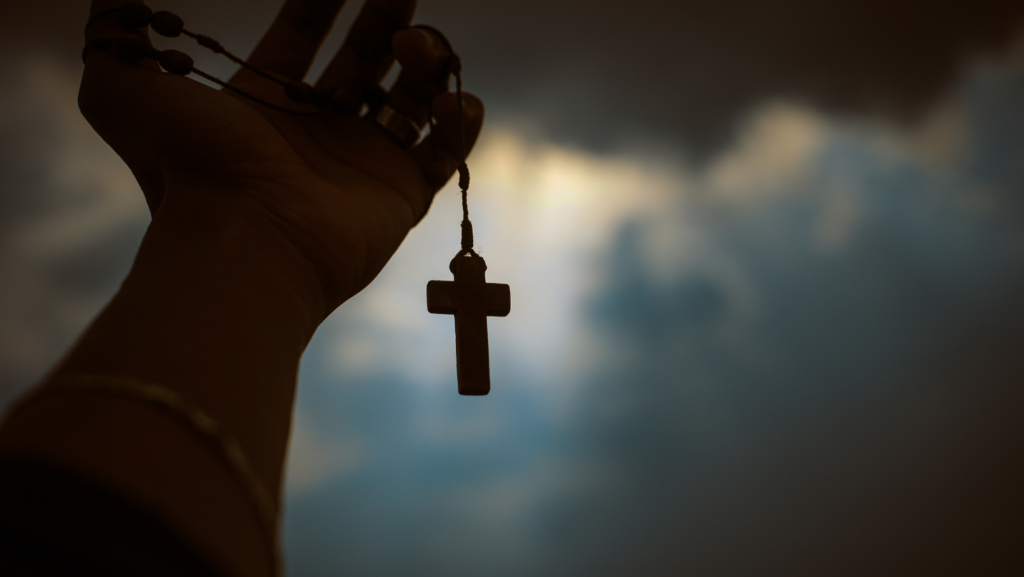 hand holding christian cross necklace with dark clouds background