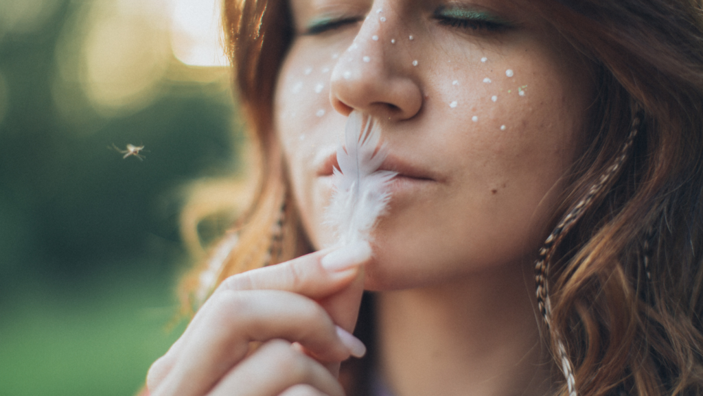 woman kissing a small white feather with her lips, eyes closed