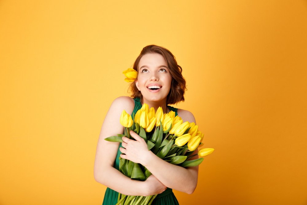 Cheerful girl with yellow flowers on yellow background