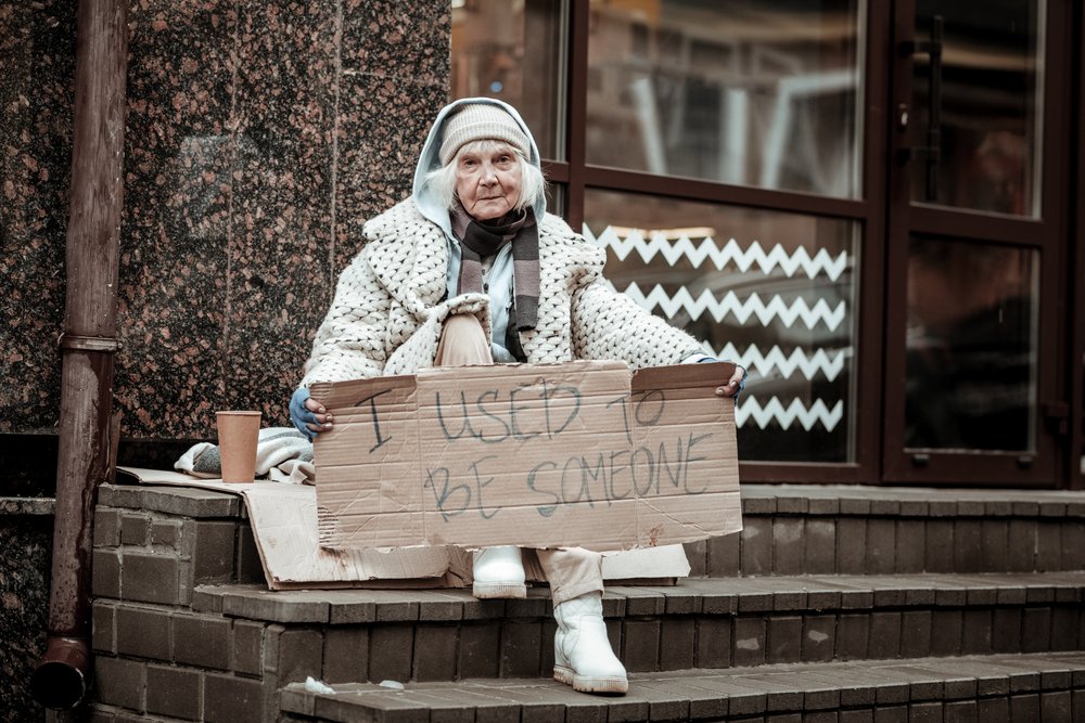 I used to be someone. Unhappy homeless woman looking at you while holding a sign in her hands